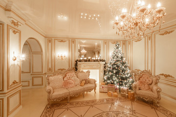 classical interior of a white room. Christmas evening by candlelight. classic apartments with a white fireplace, decorated christmas tree, sofa, large windows and chandelier.