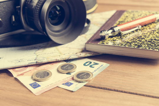 Camera, map, notebook, ball pen and money on wooden table