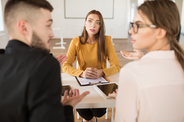 Young worry woman in blouse thoughtfully looking at employers while spending time in modern office. Female applicant waiting results of job interview