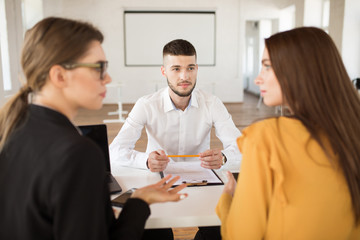 Young man in white shirt dreamily looking at employers while spending time in modern office. Male applicant waiting results of job interview