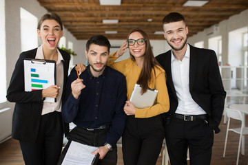 Group of cheerful creative people in suits happily looking in camera together while spending time in modern office