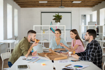 Group of young creative people eating pizza together pending time at work in modern office