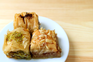 Closed up Three Types of Baklava Pastries on White Plate Served on Wooden Table, with Copy Space for Text or Design  