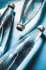 A glass bottle of water on blue background splashes drops of water on top. Quench thirst. Background of water drops - obrazy, fototapety, plakaty