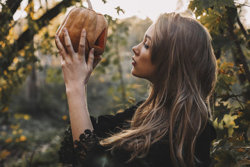 Side view of young woman holding jack o lantern in forest