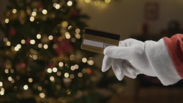 Shot of Santa holding a credit card in front of the Christmas tree