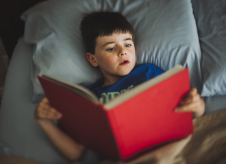High angle view of boy reading book while lying on bed at home