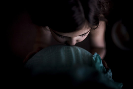 Overhead view of daughter kissing pregnant mother's belly in darkroom