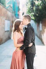 Romantic couple in Venice. Young pretty woman in rose dress and handsome man in black clothes hugging. Italy, Europe.