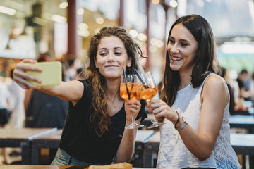 Female friends taking selfie with smart phone while toasting aperitifs in restaurant