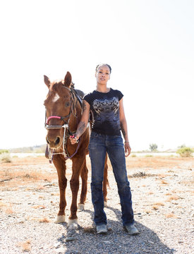 Portrait of woman standing by brown horse on dirt road against clear sky during sunny day