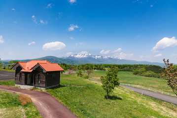 東北の高原の赤い屋根の小屋と残雪の栗駒山
