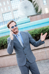 Successful young businessman wearing suit and tie talking on the phone in front of an office building. Work anywhere concept.