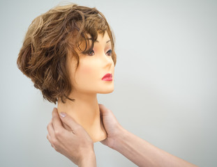 A mannequin head for teaching hairdressing in hands on a light background. Beauty concept.
