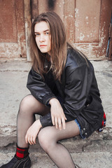 Portrait of a woman in rock, grunge style. Filmed on the street, in the open space. Dressed in a black leather jacket, shirt in red plaid. Street style and fashion.