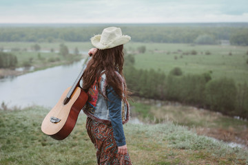 Trends dress style 2017. The concept of freedom and youth lifestyle. Girl in skirt with patterns and denim shirt in nature with guitar. Editorial use only