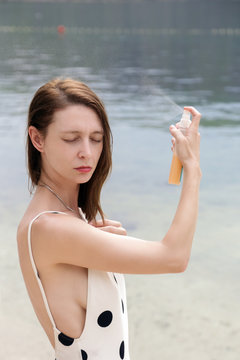 Woman applying sunscreen spray on the beach, hair care protection concept