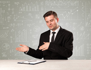 Young handsome businessman sitting at a desk with white graphs and calculations behind him 