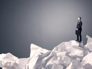 Thoughtful young businessman standing on a pile of crumpled paper with a grey background