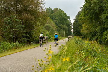 Male Cyclists on Bike Path with Trees and Bridge