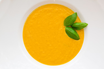 Tasty pumpkin cream soup with fresh basil leaves, blended with spice and onion. Top view, close-up.