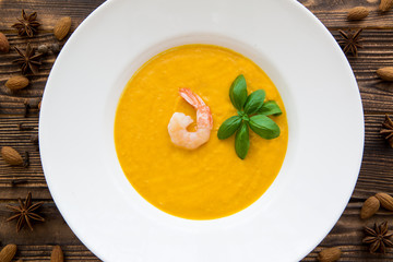 Tasty pumpkin cream soup with shrimps and basil leaves, blended with spice and carrots. Top view.