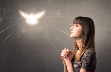 Young woman praying on a grey background with a sparkling bird above her
