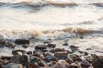 Obraz premium Ocean Waves against the rocks.Sea shock wave foam on the pebble stone beach.Sea water splash by wave on the stone beach background.Closeup of waves on the beach