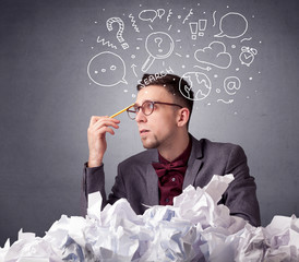 Young businessman sitting behind crumpled paper with mixed doodles over his head