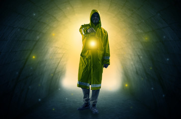 Ugly man in raincoat walking with glowing lantern in a dark tunnel