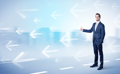 Young businessman hitchhiking near the city with arrows around concept