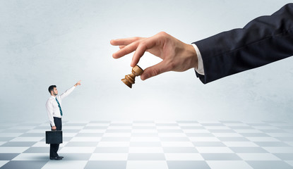 Small businessman fighting against big chessman on a big hand with chess board concept
