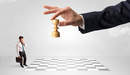 Little businessman thinking about chess strategy with a big hand concept
