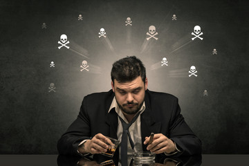 Loser drunk man sitting at table with skulls concept around
