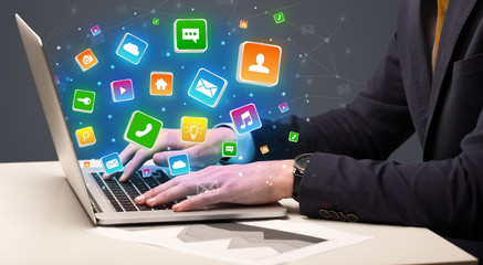 Businessman hand typing on laptop with flying application icons around
