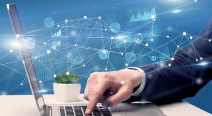 Businessman typing on laptop with linked reports charts grapghs around
