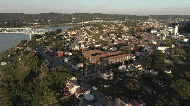An evening reverse aerial establishing shot of a small town on the Ohio River in western Pennsylvania at dusk. Pittsburgh suburbs.  	