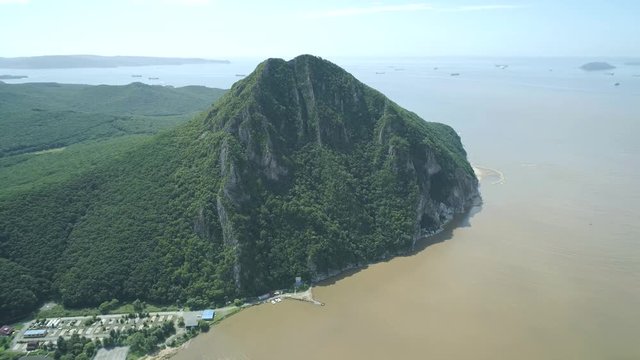Aerial view of the tall mountain covered by the forest towering over the empty valley and sea on sunny day