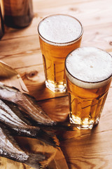 Two glasses of beer foam, bottles and dried fish on a wooden table. The view from the top