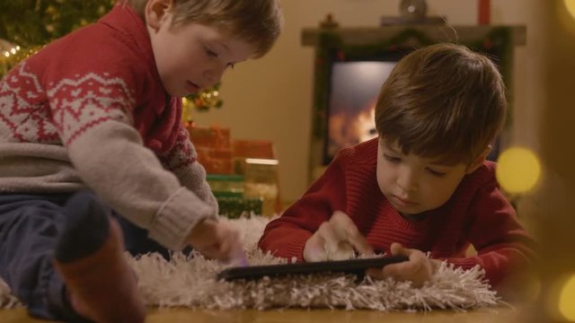 Two cute boys using the tablet in front of the Christmas tree