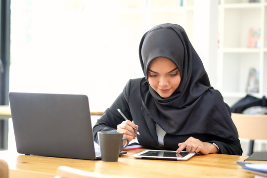 Attractive Young Asian Wearing Dark Hijab Working With Her Tablet.