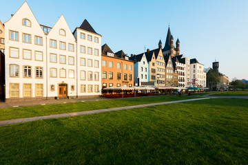 Fototapeta premium Houses and park in Cologne, Germany. Many of them are colourful, they are facing a public park with green grass and some trees. There is a Cologne bell tower on background. 