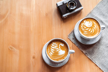two cups of cappuccino with a beautiful pattern on milk foam. Wooden table with space for text. The view from the top.