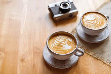 two cups of cappuccino with a beautiful pattern on milk foam. Wooden table with place for text, flower and camera, retro . The view from the top