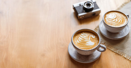 two cups of cappuccino with a beautiful pattern on milk foam. Wooden table with place for text, flower and camera, retro . The view from the top