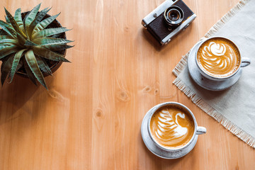 two cups of cappuccino with a beautiful pattern on milk foam. Wooden table with place for text, flower and camera, retro . The view from the top