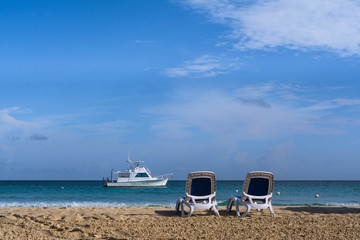 Dos sillas de playa est&aacute;n en la arena muy cerca del barco.