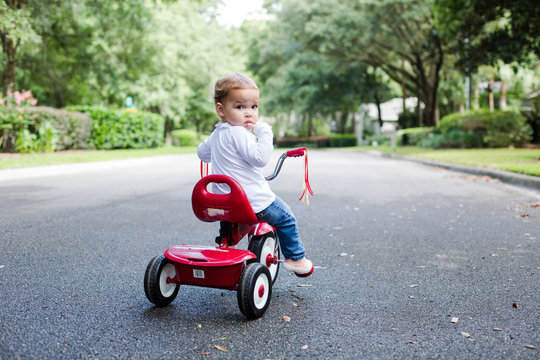 Young Child Toddler on Red Tricycle on a Neighborhood Street Looking at Camera