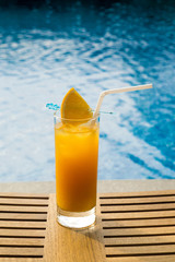 Orange juice in a glass on the wooden table by the pool. Juice