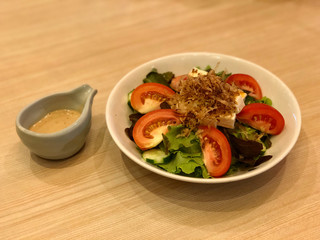 Tofu Salad topped with small crispy fish dish and White sesame dressing on the wooden table.Healthy menu for diet. Traditional Japanese food salad. top view and copy space